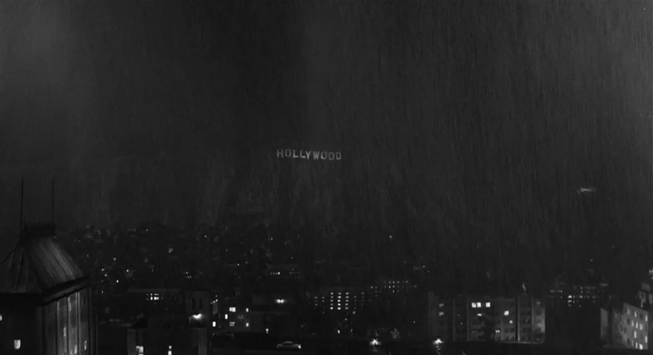Ed Wood (1994) movie still: establishing — A night time city landscape is obscured by a heavy downpour of rain. The illuminated Hollywood sign sits…
