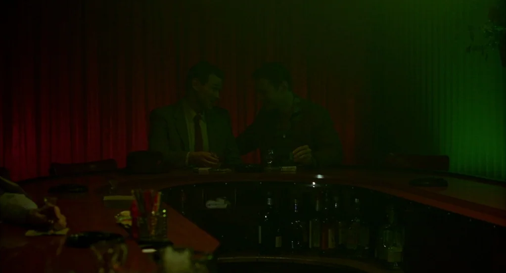 Far From Heaven (2002) movie still: medium — A dimly lit lounge featuring a curved counter and walls draped in dark curtains. Two men sit close…