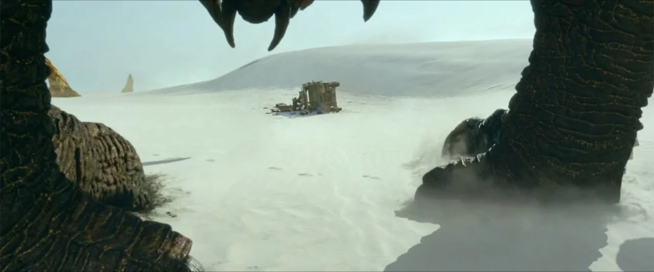 Monster Hunter (2020) movie still: wide — A vast, bright white sand desert stretches toward a distant overturned vehicle. The perspective is from…