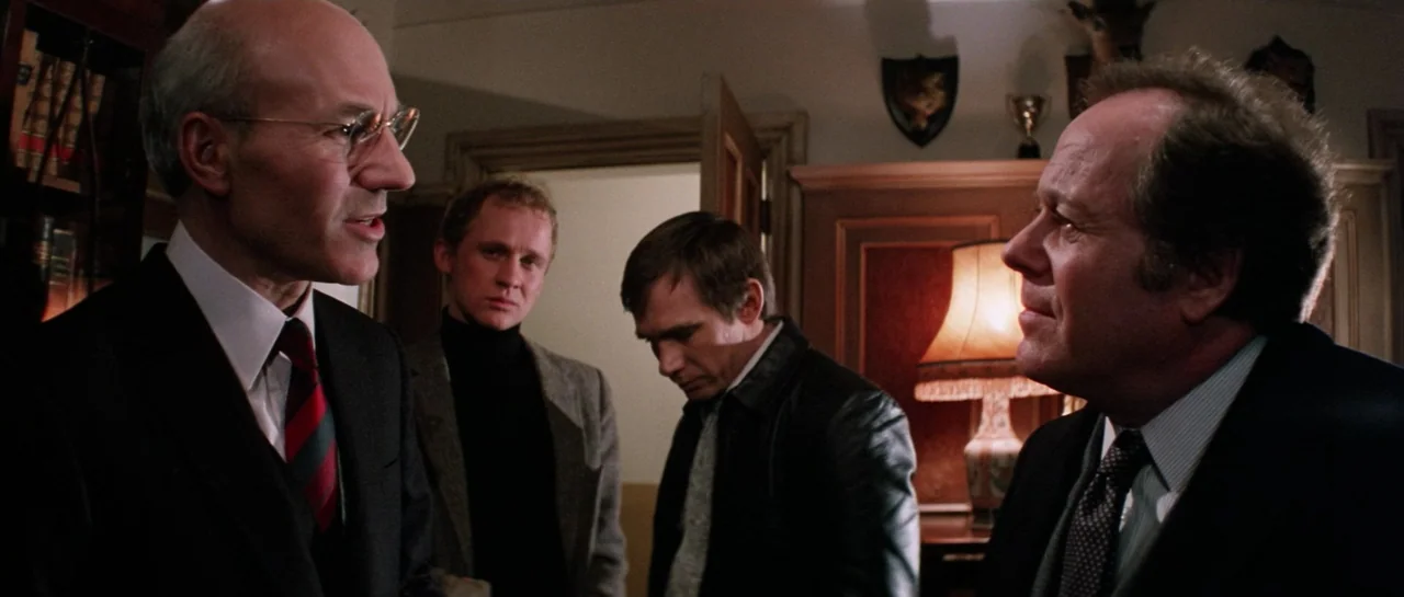 Lifeforce (1985) movie still: medium — A wood-paneled room containing taxidermy mounts and a table lamp with a fringed shade. Two men face each…