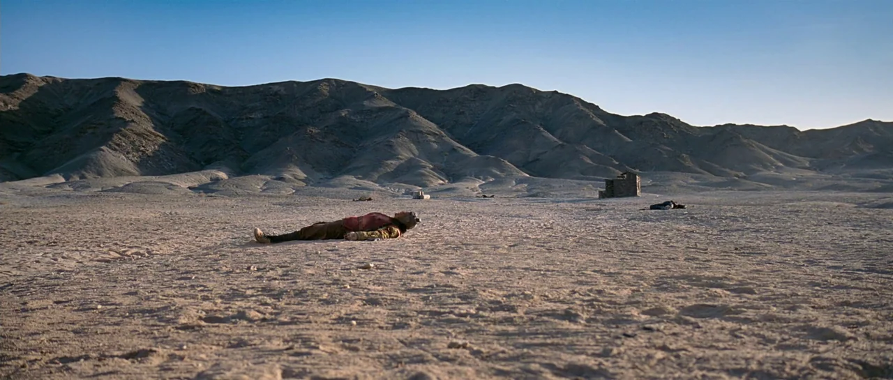 The Good The Bad The Weird (2008) movie still: wide — A vast, barren desert stretches toward rugged, dry mountain ranges under a clear sky. A figure…