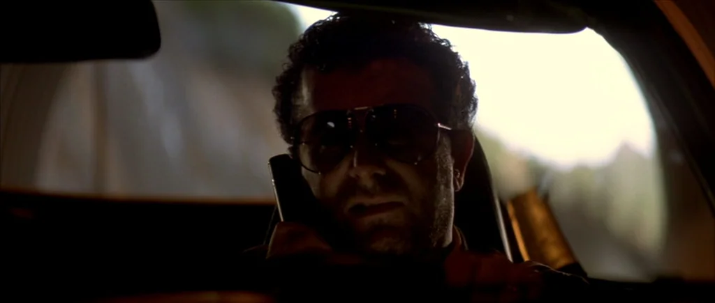 True Romance (1993) movie still: closeup — The interior of a moving vehicle shows the driver partially obscured by heavy shadow. He holds a portable…