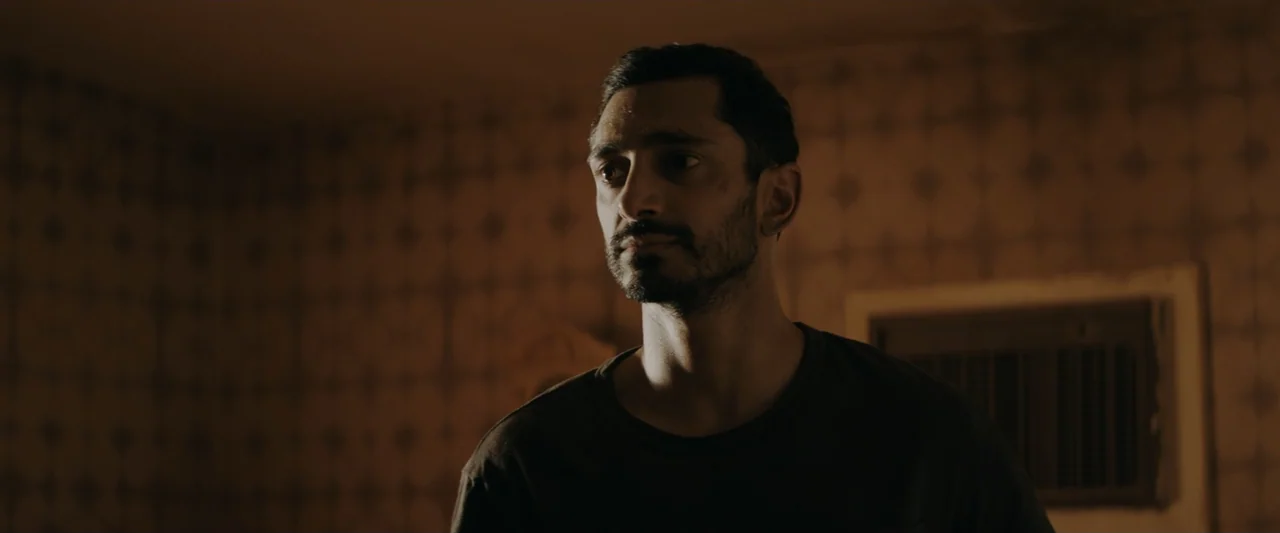 Encounter (2018) movie still: medium — A dimly lit interior space features walls covered in vintage patterned wallpaper. A man in a dark t-shirt…