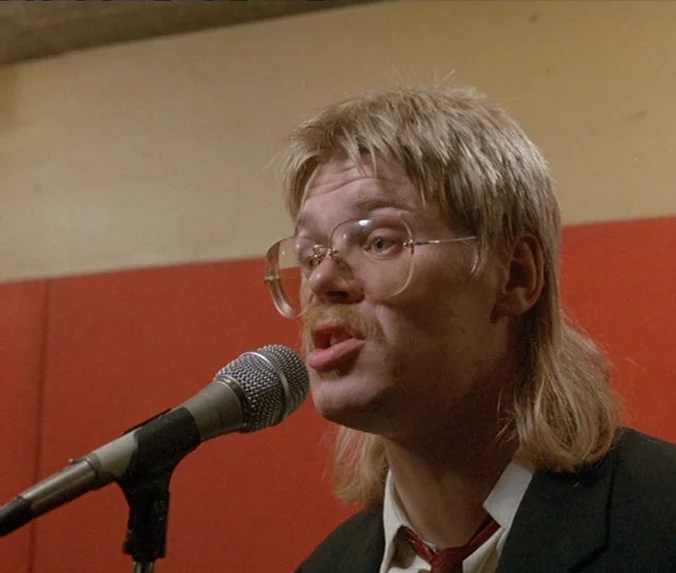 Crime & Punishment (1983) movie still: closeup — A recording studio with plain red soundproofing panels covering the back wall. A man with a blonde…