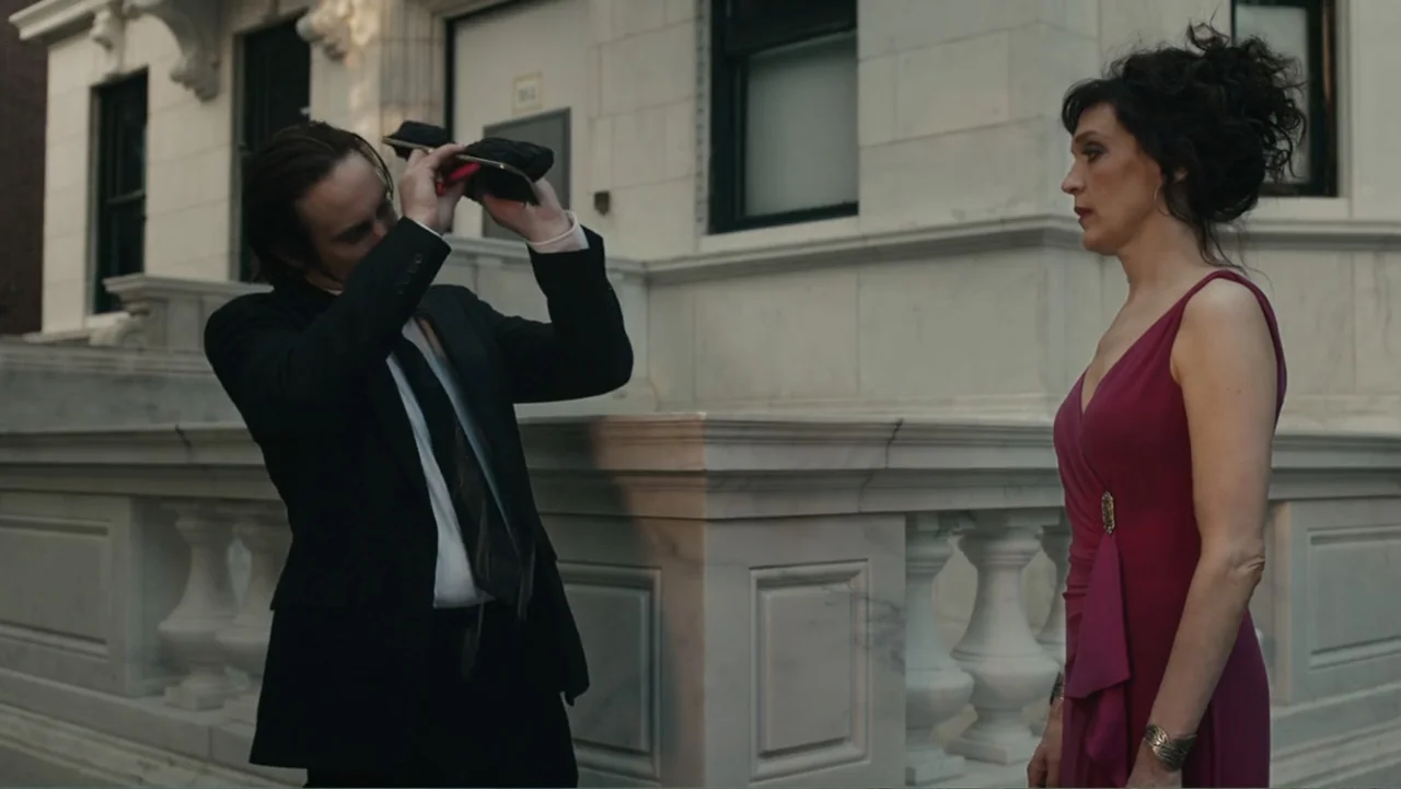 Toss It (2019) movie still: medium — A stone townhouse exterior with a white balustrade and large building entrance background. A man in a suit…