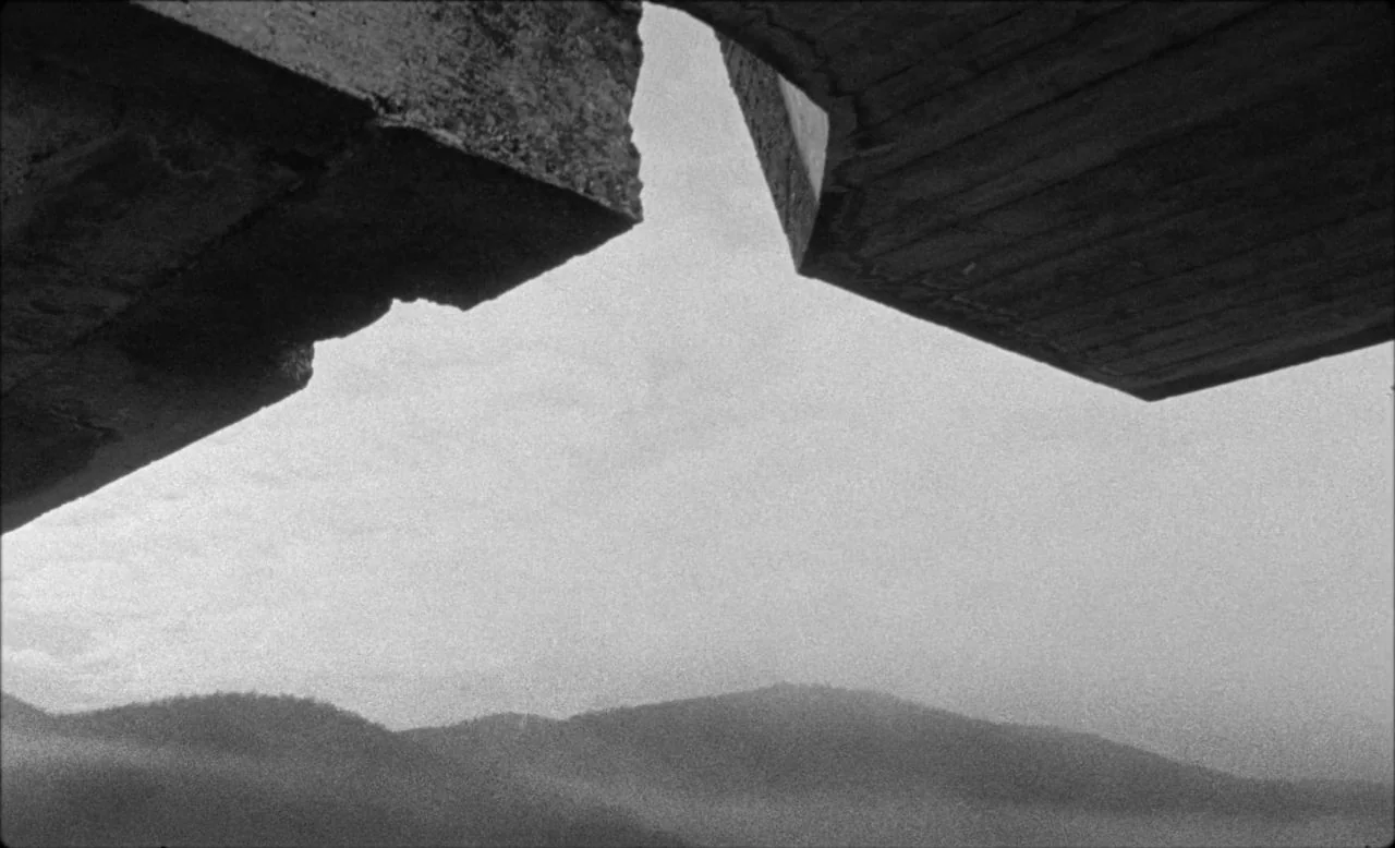 Last and First Men (2020) movie still: establishing — A view of hazy mountain ridges seen from underneath a concrete architectural structure. The…