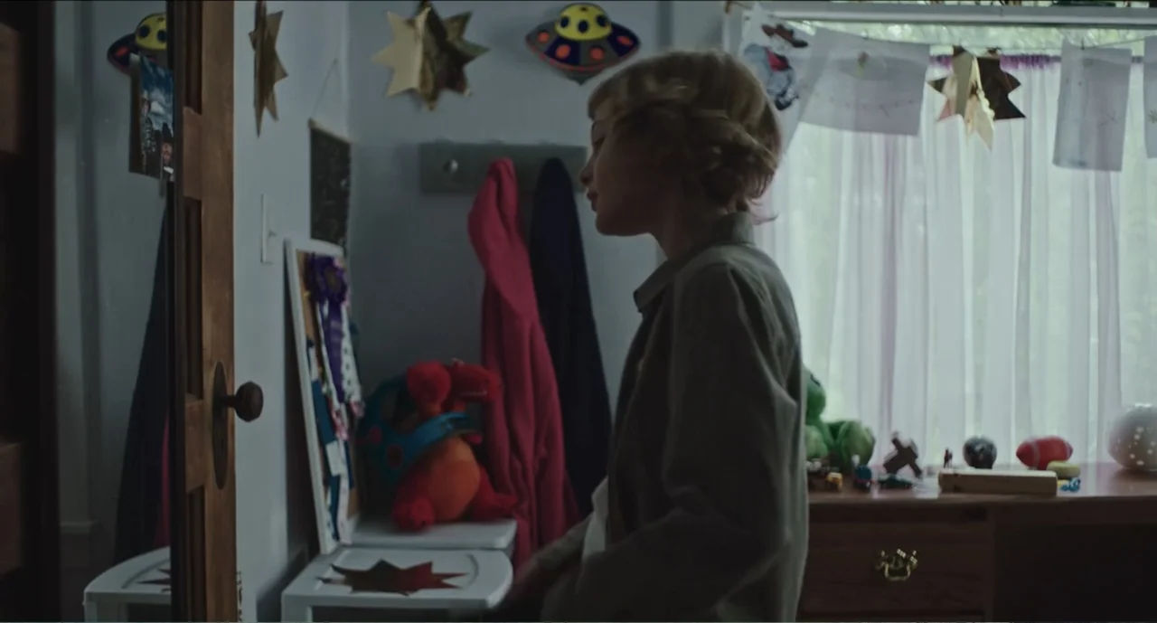 Cowboys (2014) movie still: medium — A child's bedroom contains toys, wall decorations including a UFO sign, and a wooden desk. The boy stands in…
