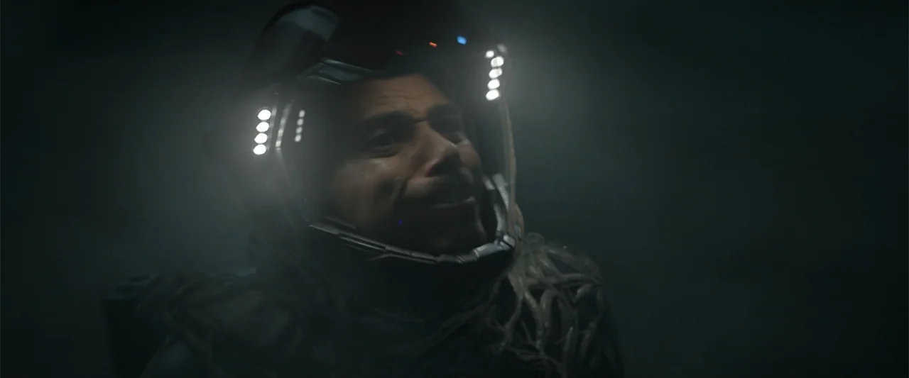 DISTANT (2026) movie still: closeup — The interior of a dark, dimly lit cockpit features a person in space gear. The individual wears a glowing…