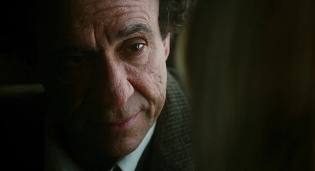 Mimic (1997) movie still: closeup — The interior of a vehicle is shrouded in darkness during the evening. An older man gazes toward the window with…