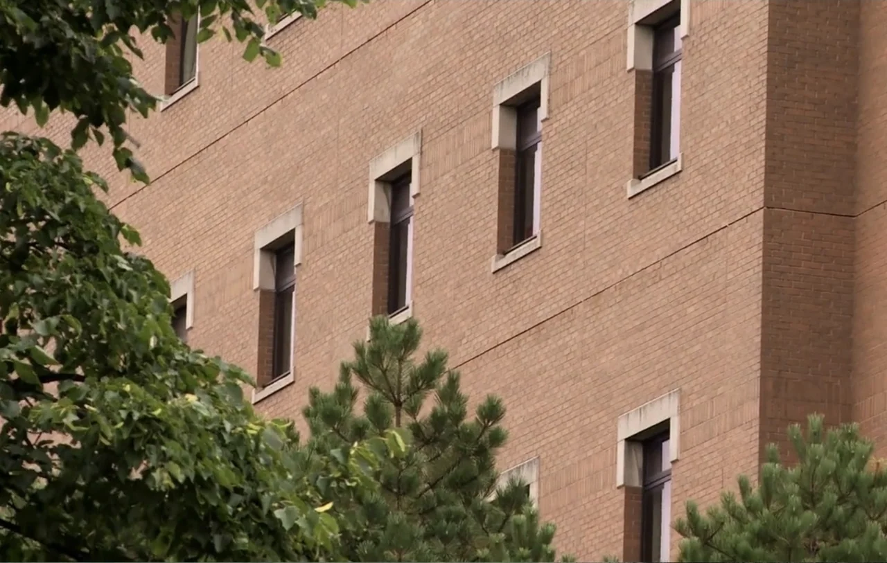 No Place to Hide (1992) movie still: establishing — A multi-story tan brick building facade features evenly spaced windows with simple stone…