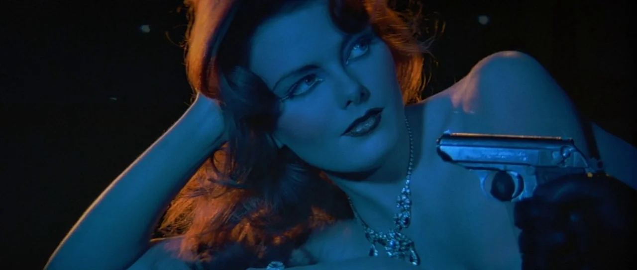 Octopussy (1983) movie still: closeup — A dark space lit by high-contrast blue and orange lighting. A woman lies down while aiming a small pistol…