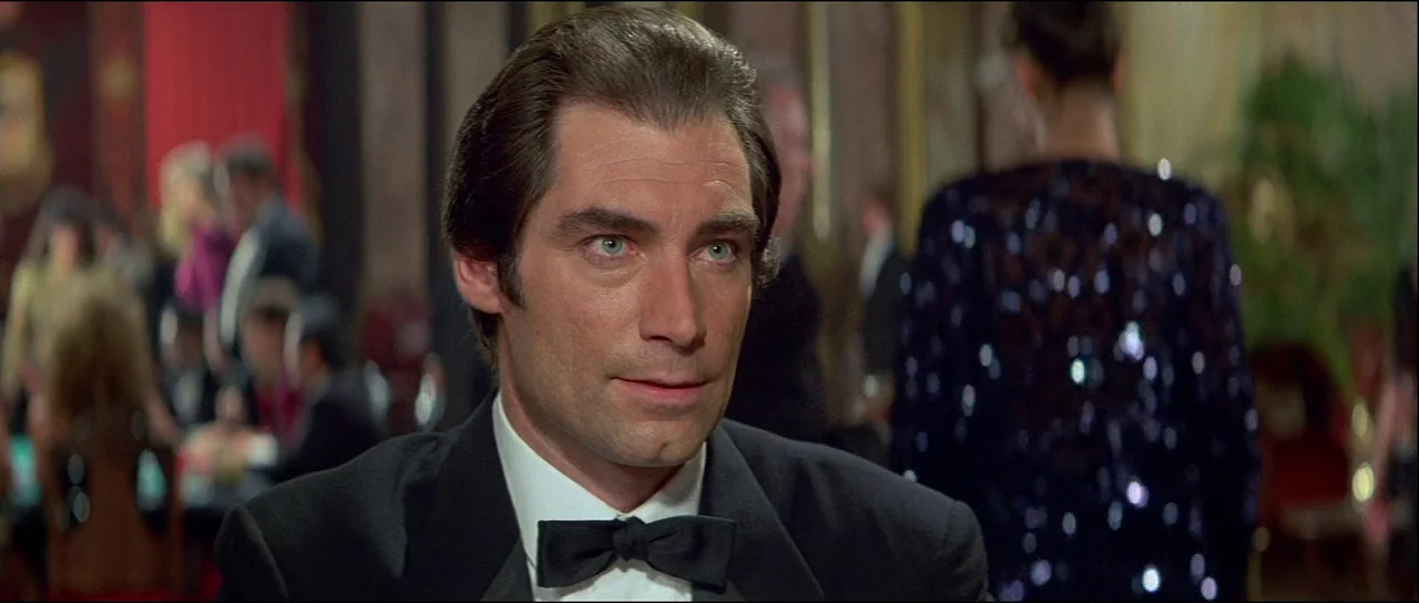Licence to Kill (1989) movie still: closeup — A well-lit indoor space filled with patrons sitting at tables. The foreground subject wears formal…