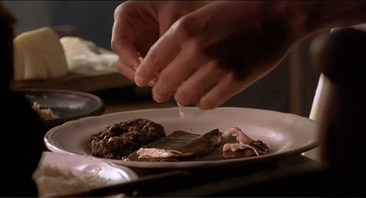 Like Water for Chocolate (1992) movie still: closeup — A domestic dining setting with a ceramic plate containing food. Hands appear in the frame…
