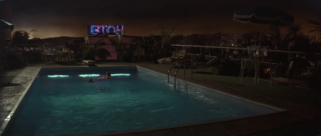Pink Floyd The Wall (1982) movie still: wide — A dark, rectangular pool occupies a rooftop terrace overlooking a sprawling city at night. A lone…