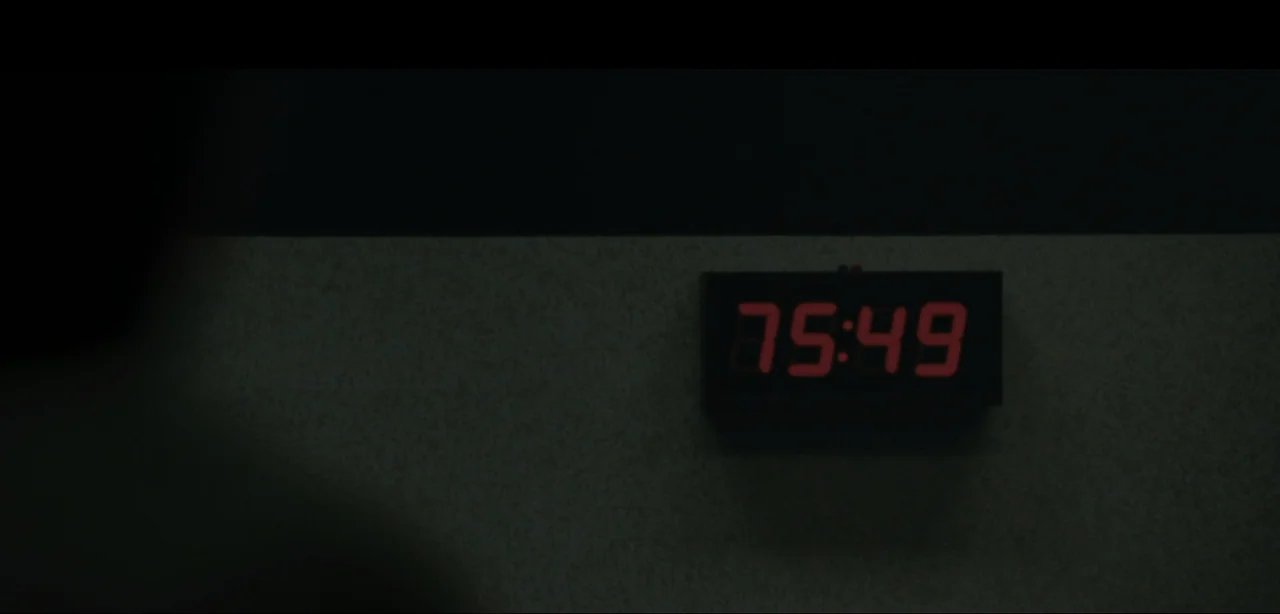 Slackers (2002) movie still: closeup — A dimly lit room features a glowing digital clock mounted on a wall. The device displays a red timer counting…