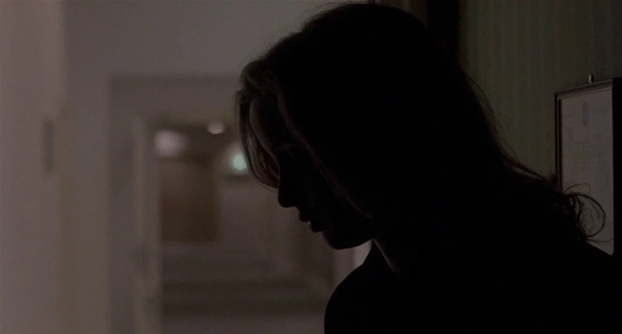 Three Colours: White (1994) movie still: closeup — A dimly lit indoor hallway with a doorway visible in the background. A woman in silhouette stands…