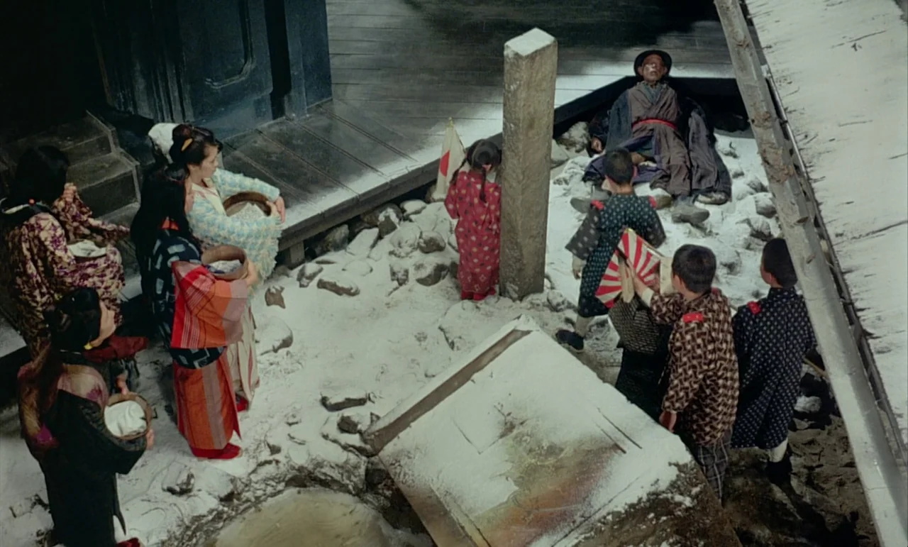 In The Realm of the Senses (1976) movie still: wide — A snowy courtyard in Japan features an elderly man sitting on the ground. A group of women and…