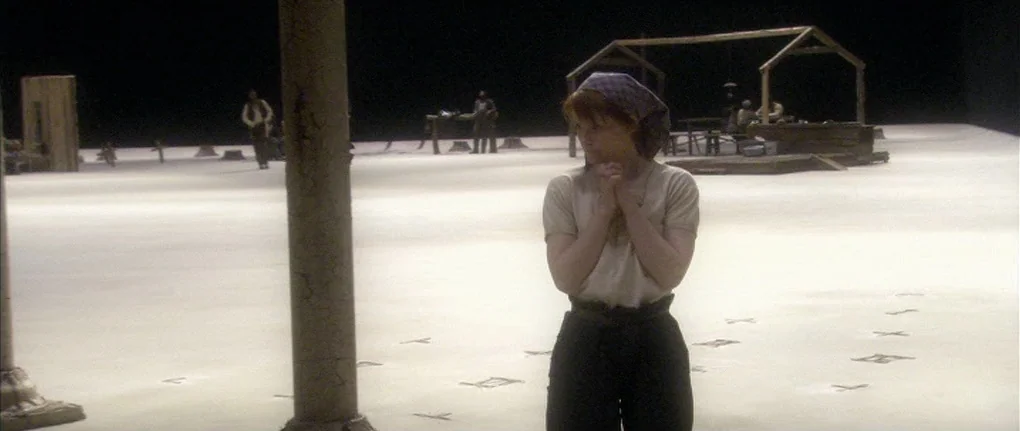 Manderlay (2005) movie still: medium — A minimalist theatrical set features a vast, light-colored floor against a black void. A woman stands…