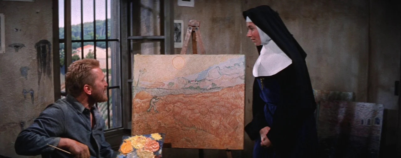 Lust For Life (1956) movie still: medium — A rustic studio with textured walls and an easel holding an orange-toned landscape painting. A bearded…