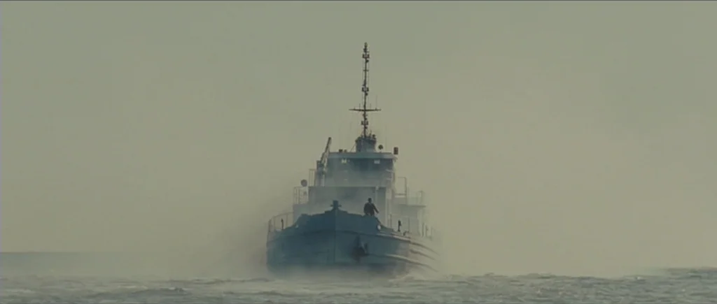 Shutter Island (2010) movie still: wide — A naval patrol boat navigates through choppy grey water under an overcast sky. The vessel displaces spray…