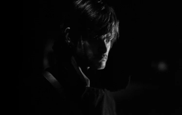 Werckmeister Harmonies (2000) movie still: closeup — A dark, featureless environment surrounds a man's face caught in a pool of light. He stands…