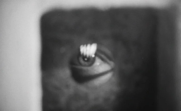 The Cremator (1969) movie still: closeup — A dark abstract frame features a single human eye at the center. The surrounding area is obscured in…