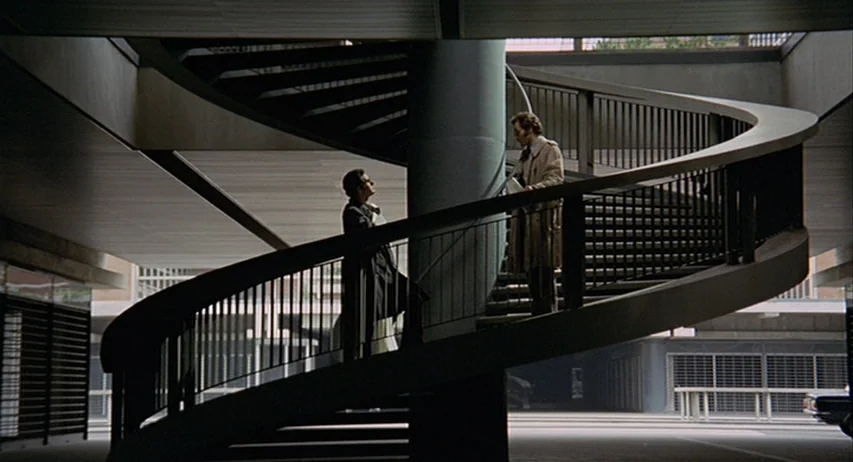 The Fifth Cord (1971) movie still: wide — An outdoor concrete structure features a large, sculptural spiral staircase between two modern buildings.…