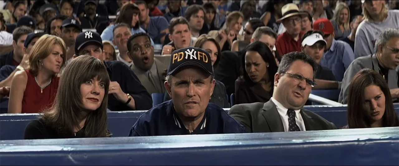 Anger Management (2003) movie still: medium — A crowded stadium section with spectators watching a game from blue bench seating. A group of people…