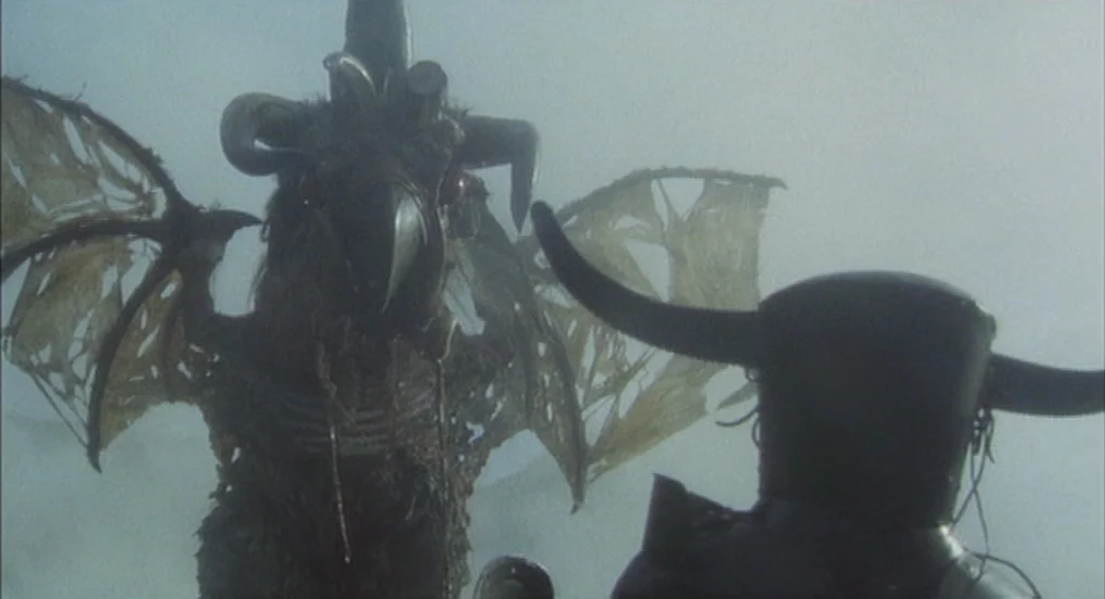 Jabberwocky (1977) movie still: medium — A dark winged creature confronts a knight wearing a horned helmet in thick fog. The scene is set in an…