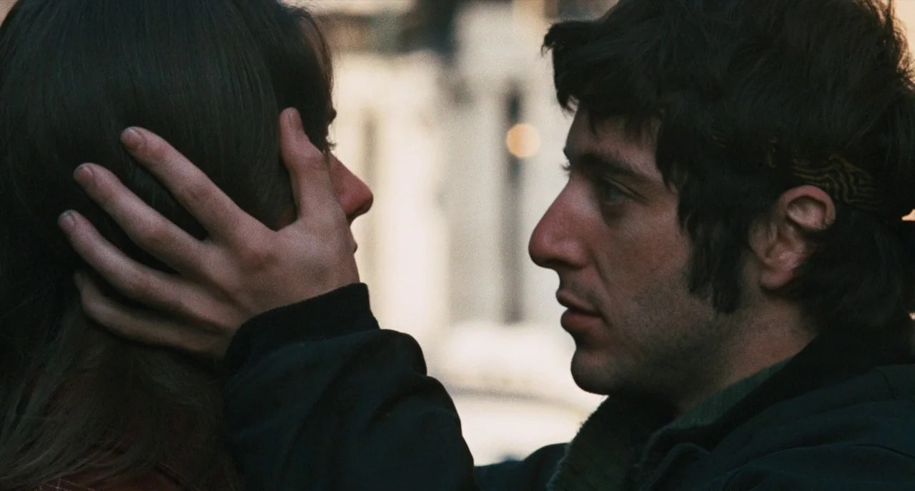The Panic in Needle Park (1971) movie still: closeup — A close-up view of two individuals standing on an urban street. The man holds the woman's…