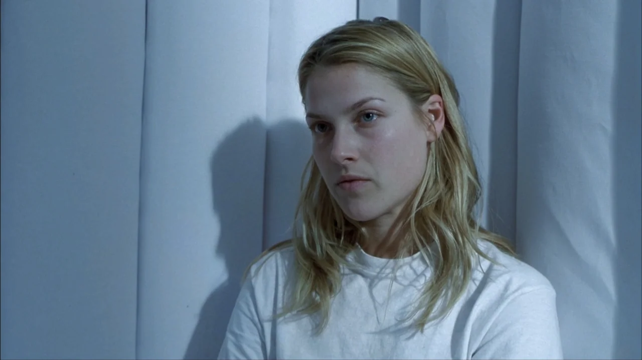 Final Destination 2 (2003) movie still: medium — A woman stands before white fabric curtains in a dimly lit indoor space. She looks off-camera while…