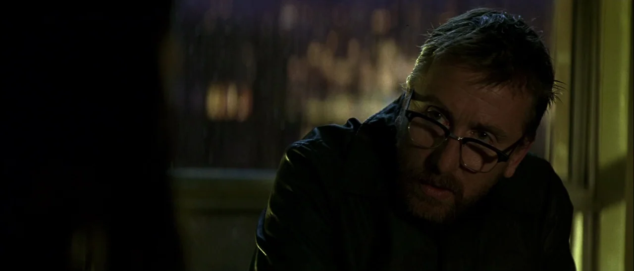 Dark Water (2005) movie still: closeup — A dark indoor setting features a man in focus near a window at night. The man wearing glasses looks toward…