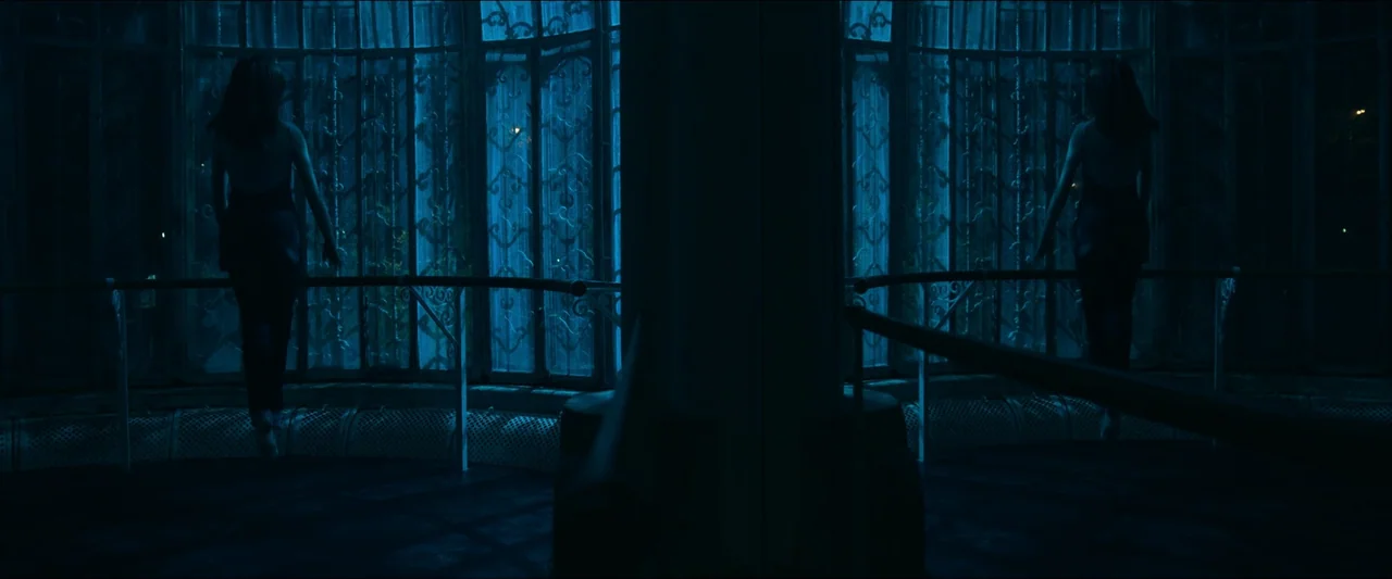 Birds of Paradise (2021) movie still: wide — A dark dance studio features a curved wall of large multi-paned windows at night. A female dancer in a…