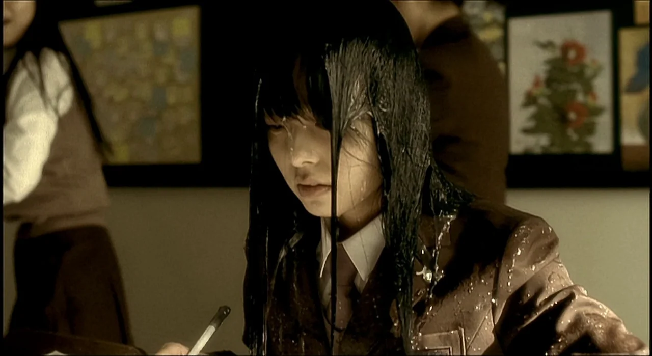 Voice (2005) movie still: medium — A school classroom featuring posters on the back wall and students at desks. A female student with soaked hair…