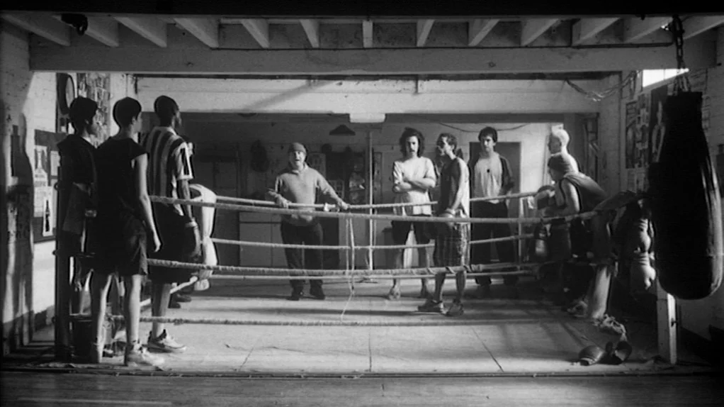 TwentyFourSeven (1997) movie still: wide — A basement level boxing training facility with low ceilings and exposed wooden beams. A group of men…