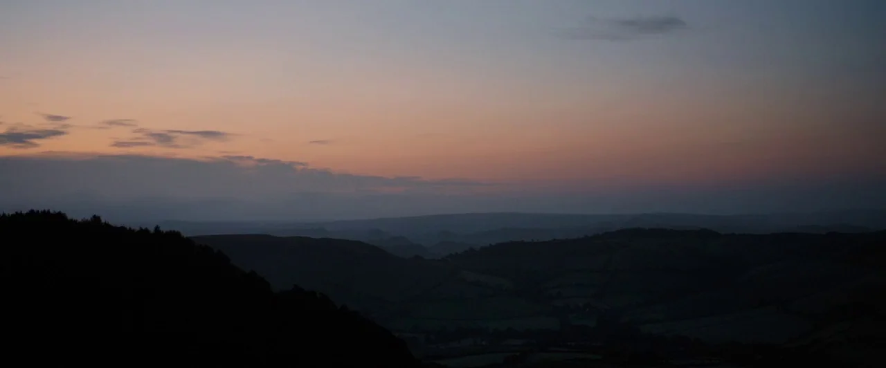 Far from the Madding Crowd (2015) movie still: establishing — A wide view of dark, silhouetted rolling hills under a gradient evening sky. Small…