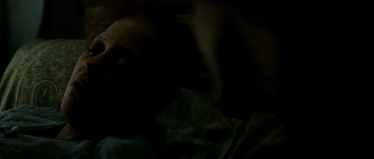 La Vie En Rose (2007) movie still: closeup — A dimly lit room with an older woman lying on a paisley patterned pillow. The subject rests her head on…