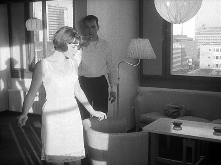 Masculin Féminin (1966) movie still: medium — A modern 1960s interior features large windows overlooking an urban cityscape and minimalist…