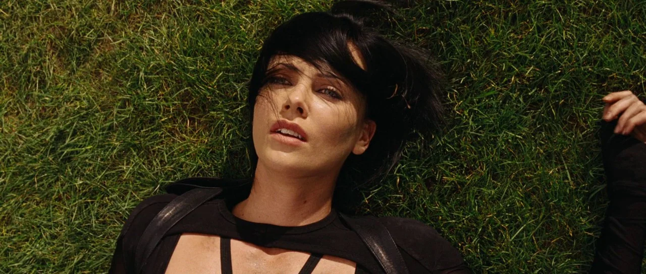 Aeon Flux (2005) movie still: closeup — A woman lies on a patch of lush green grass. She is positioned on her back and looking directly into the…