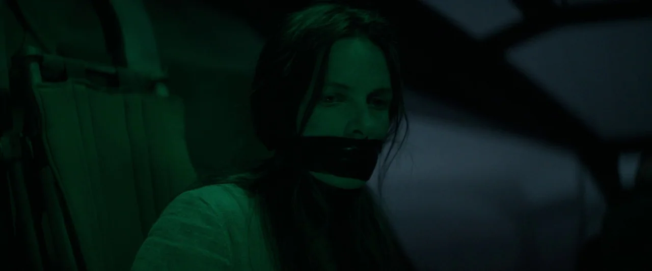 Dune (2021) movie still: closeup — A dark vehicle cabin lit with green monochrome light. A woman sits bound with duct tape across her mouth.