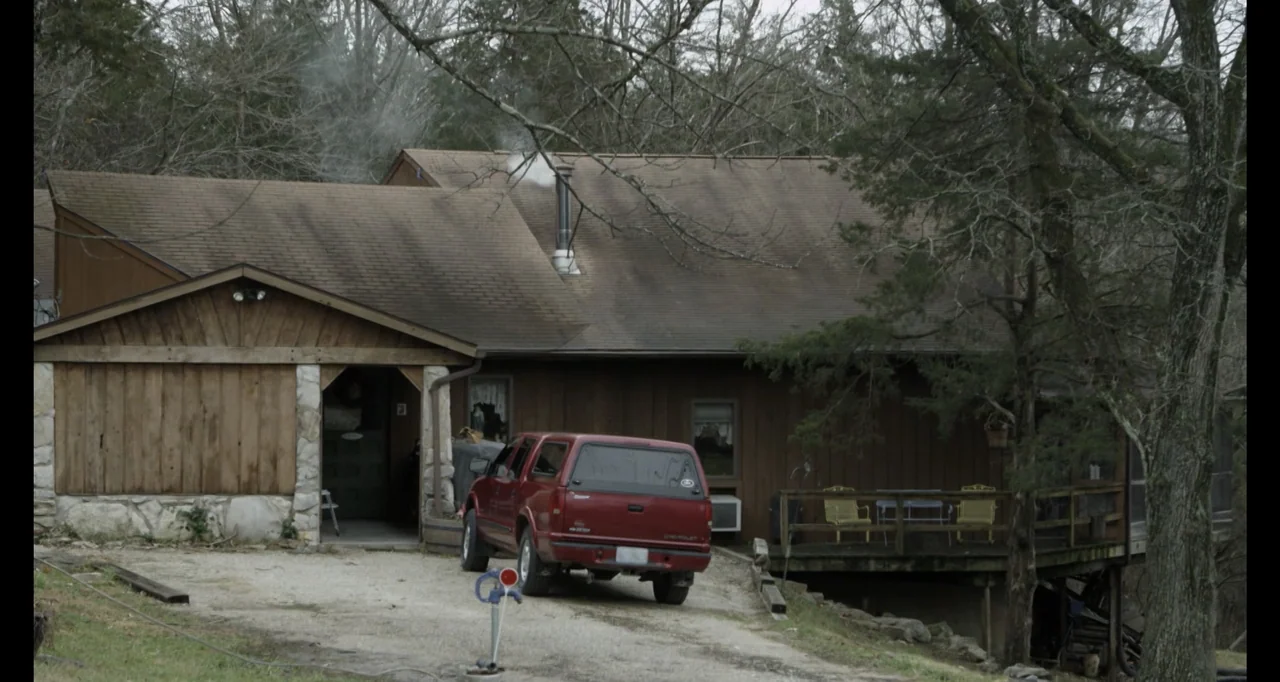 Abortion: Stories Women Tell (2016) movie still: wide — A wooden rustic house with a red truck parked in the driveway. Trees surround the structure…