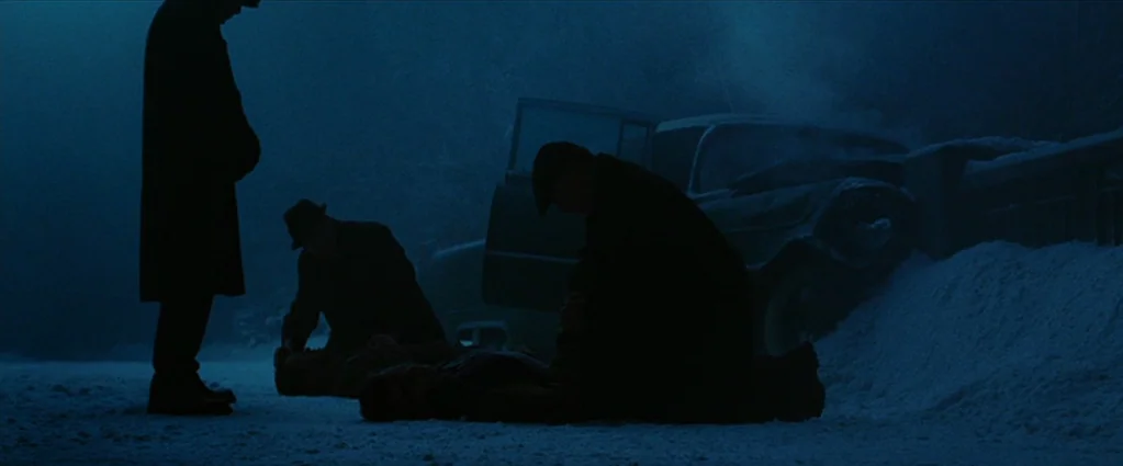 Wind Chill (2007) movie still: wide — A snowy roadside at night features a dark car stalled near a bank of snow. Three men in long coats surround a…