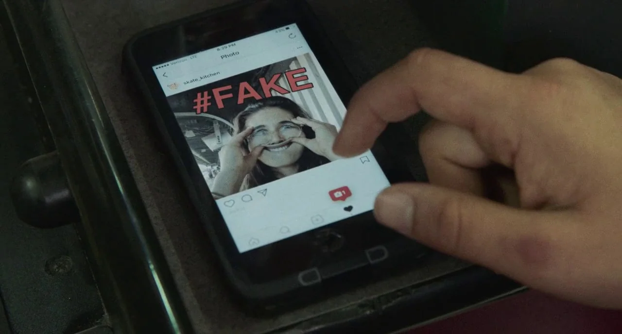 Skate Kitchen (2018) movie still: closeup — A close-up of a smartphone screen held in a hand inside a vehicle. The screen shows a social media post…