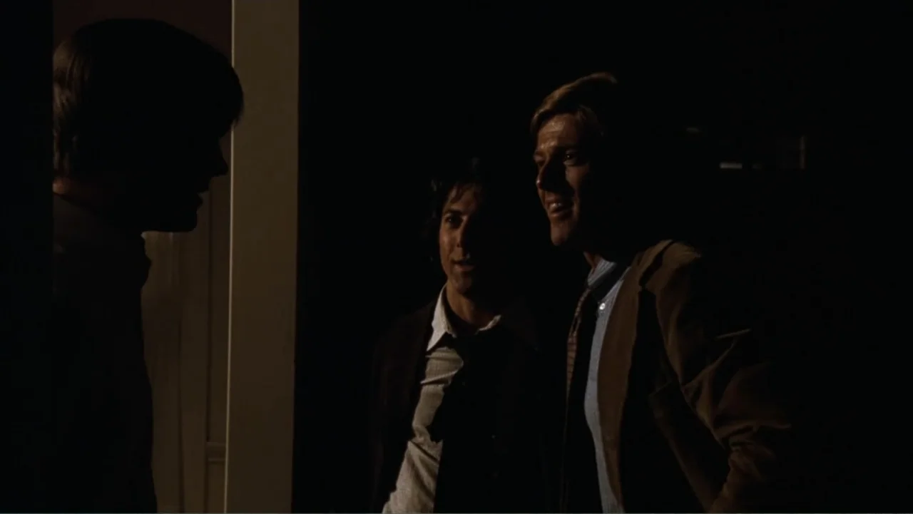 All the President's Men (1976) movie still: medium — A dimly lit entryway features three men interacting at the threshold of a doorway. Two men in…