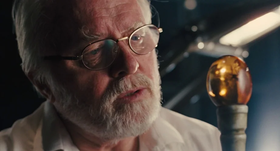 Jurassic Park (1993) movie still: closeup — An older man stands in a dimly lit laboratory space holding an object. He observes a glowing…