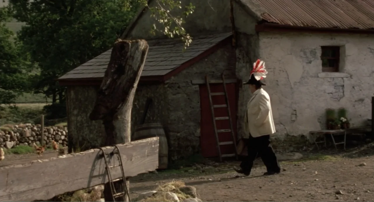 Dancing at Lughnasa (1998) movie still: fullbody — An aged stone outbuilding with a corrugated roof sits next to a dirt path. A man in a light…