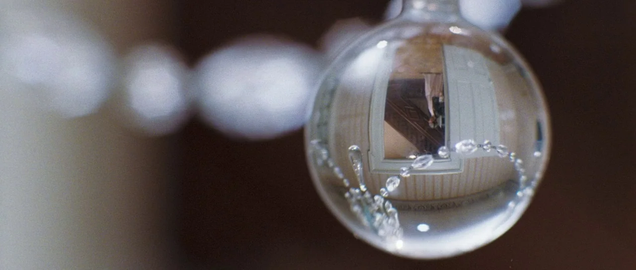 Stay (2005) movie still: closeup — A close-up view shows a circular crystal bead catching a reflection of a hallway. A narrow doorway and a…