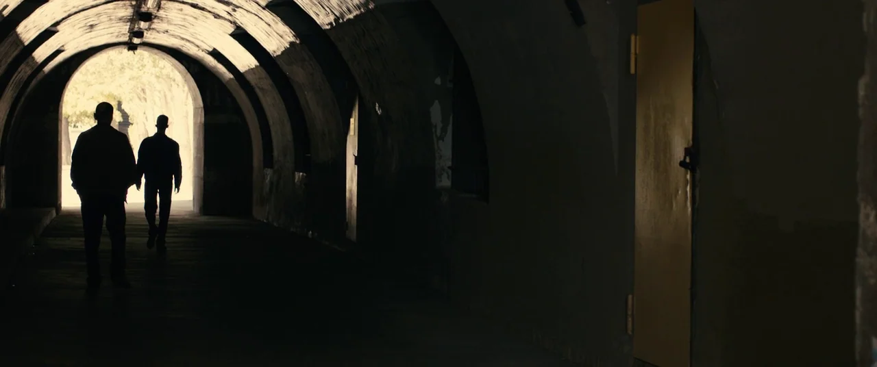 BPM (Beats Per Minute) (2017) movie still: wide — A stone tunnel with arched ceiling and a solitary light-colored door set in the wall. Two men walk…