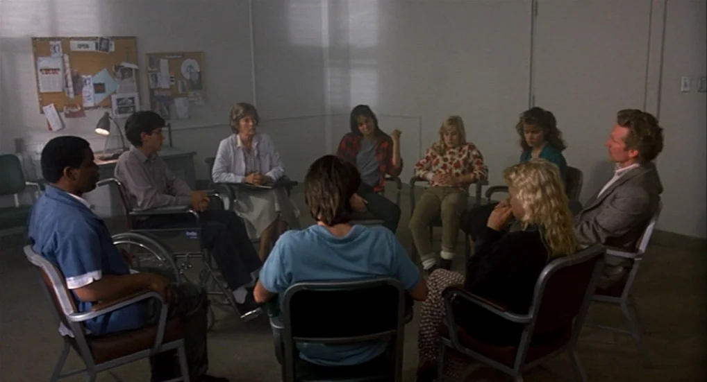 A Nightmare On Elm Street 3: Dream Warriors (1987) movie still: wide — A group of eight people sits in a circle within a plain white room. They…
