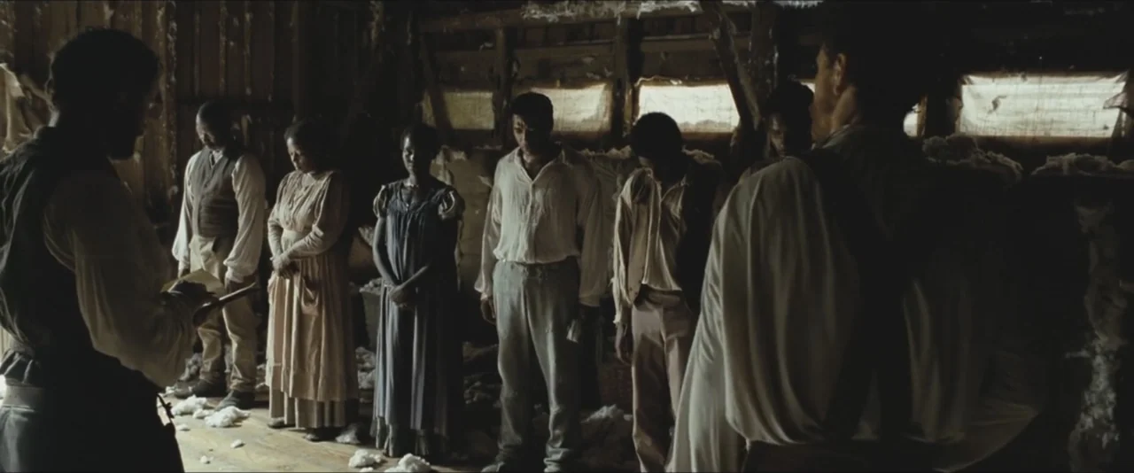 12 Years a Slave (2013) movie still: fullbody — A rustic wooden barn interior features rough timber walls and scattered raw cotton fibers. Multiple…